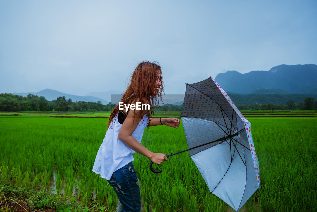 Smiling woman with umbrella standing on field