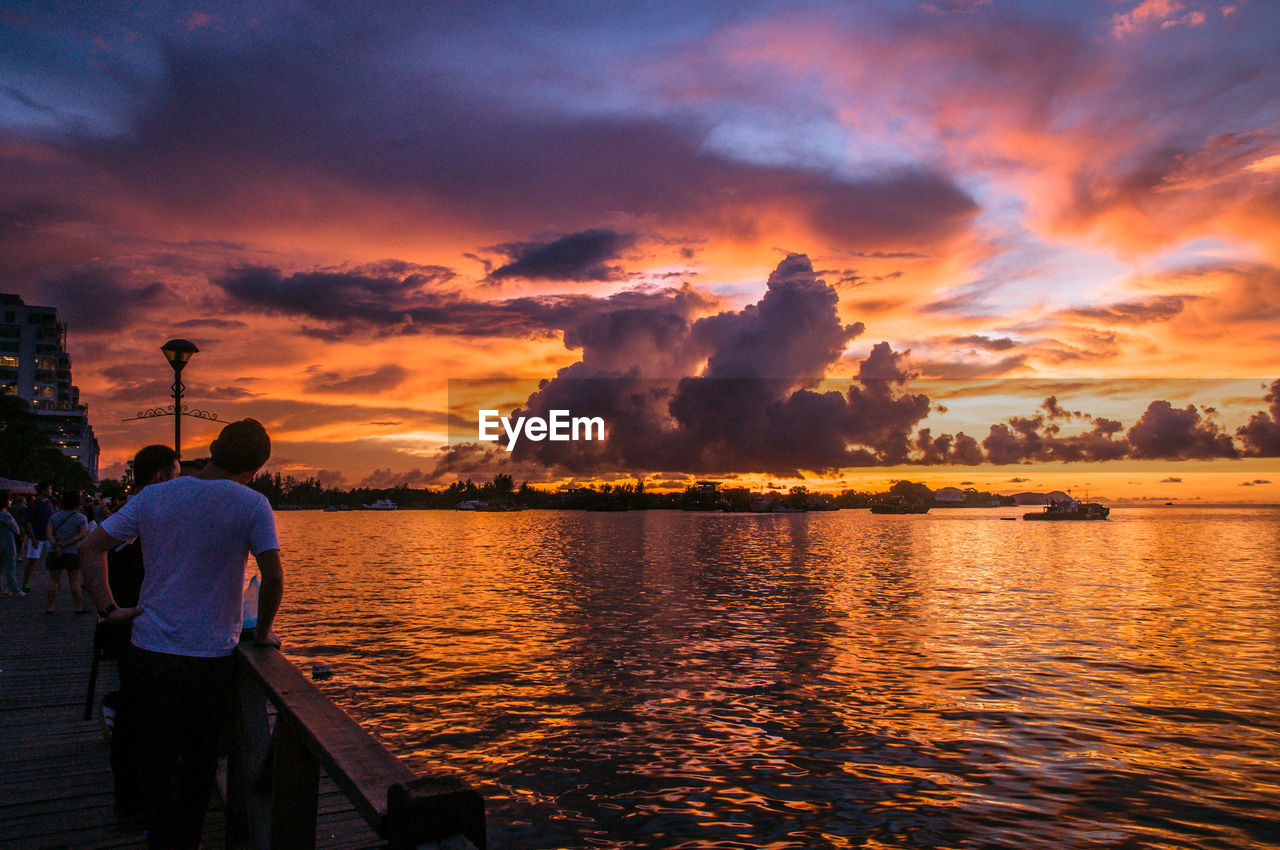 People standing on pier by sea against sky during sunset