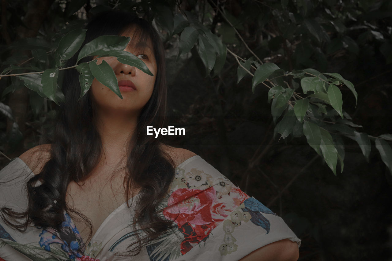 Woman looking away while standing against plants