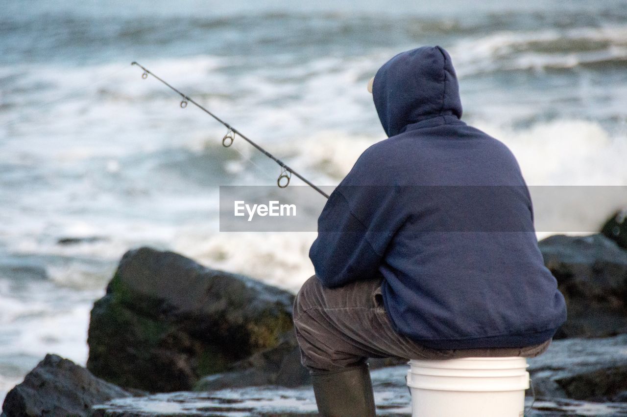 REAR VIEW OF MAN FISHING AT SEA