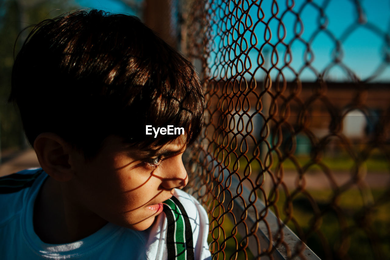 Close-up f boy looking through chainlink fence