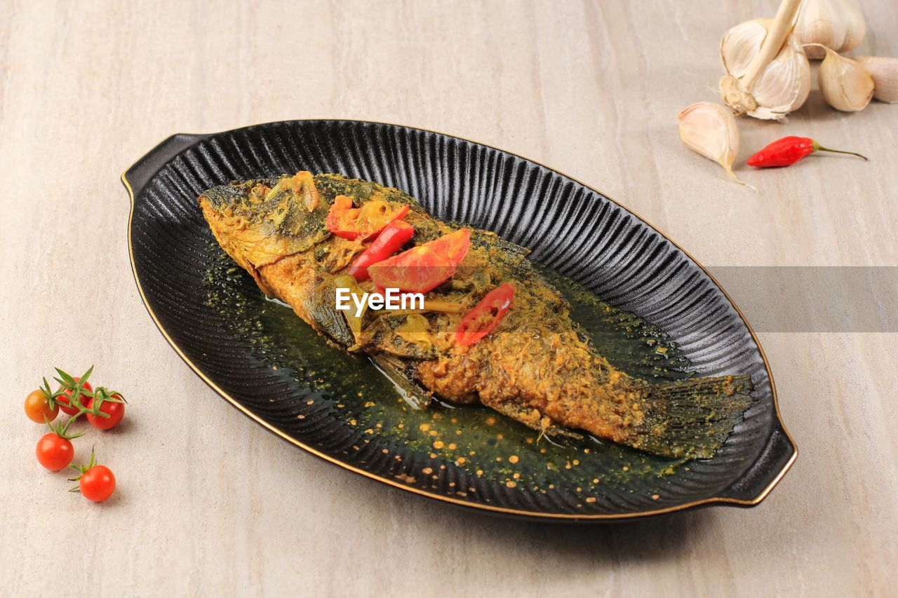 Ikan pesmol or pesmol fish with yellow curry, close up on wooden table with copy space for text