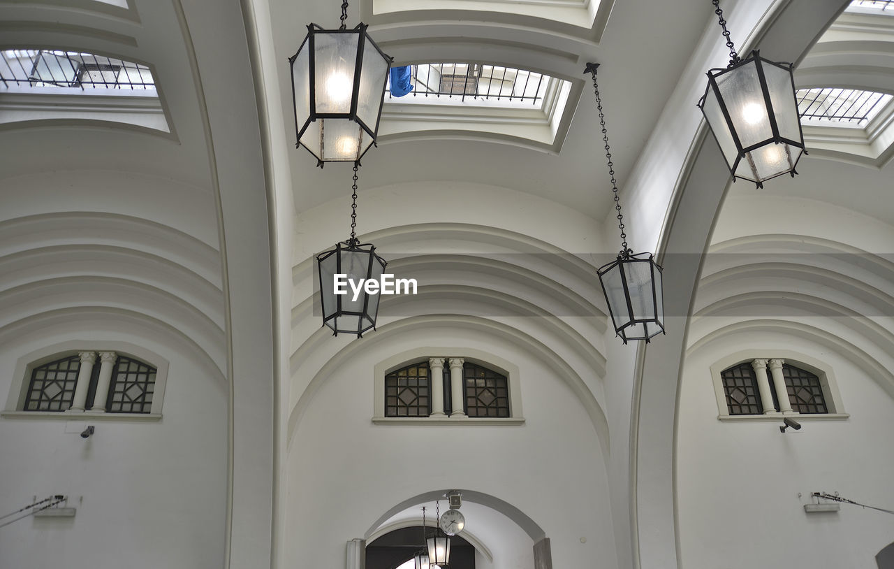LOW ANGLE VIEW OF ILLUMINATED PENDANT LIGHTS HANGING IN BUILDING