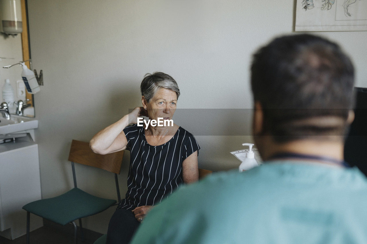 Senior woman touching neck while discussing with doctor in clinic