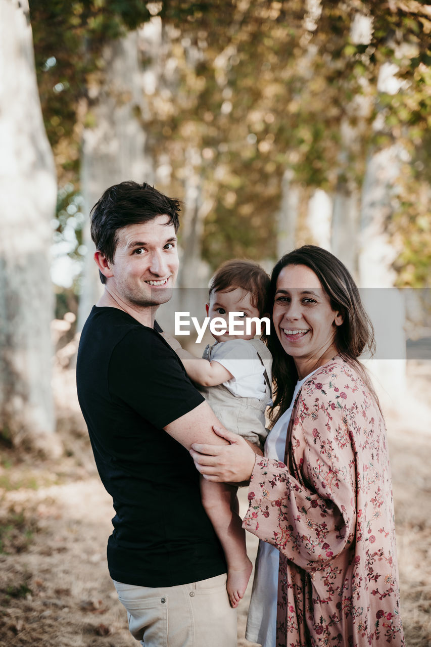 Smiling father carrying baby while standing by mother outdoors