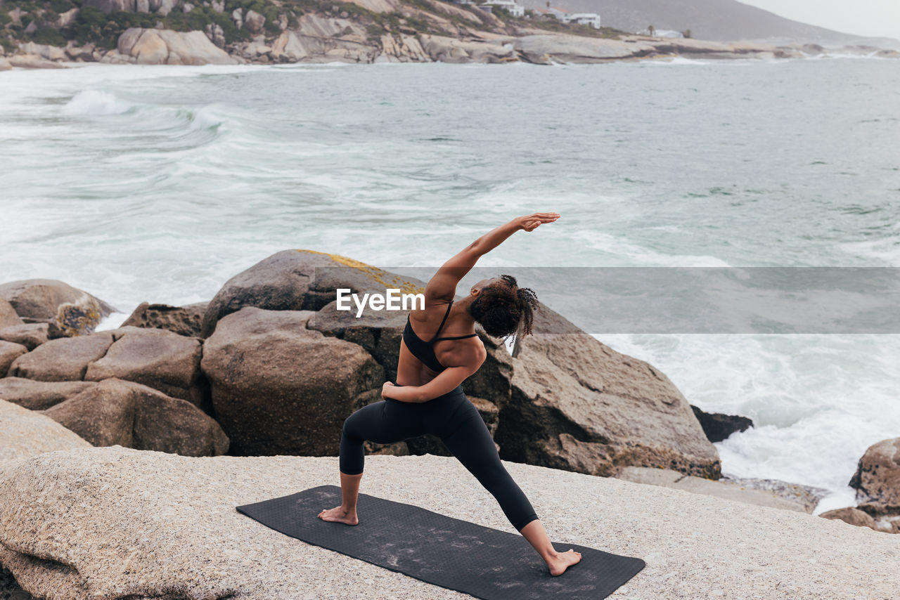 side view of woman doing yoga on rock at beach