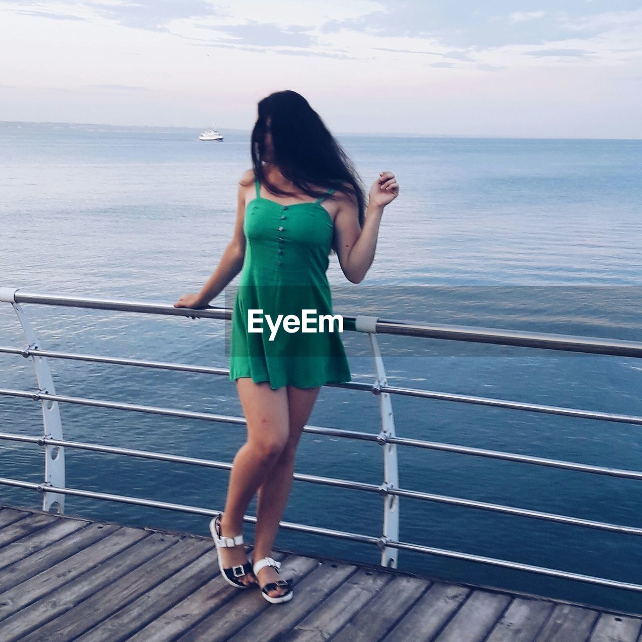 Young woman standing by railing against sea