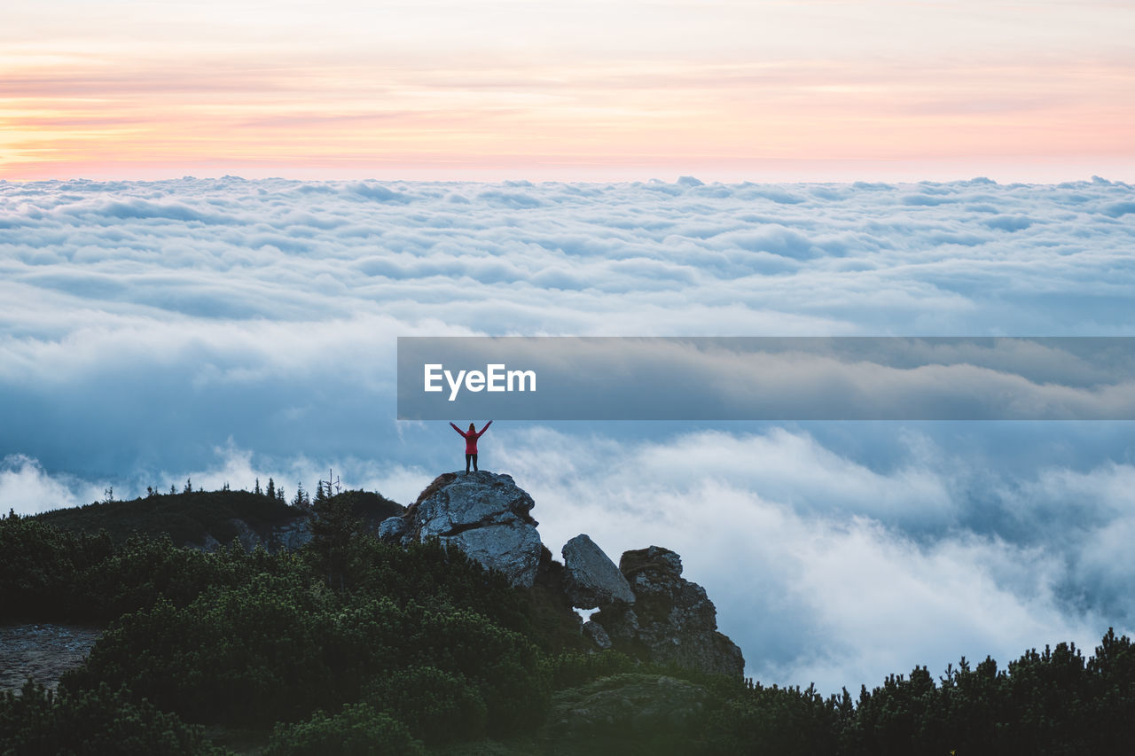 MAN STANDING ON ROCK AGAINST SKY AT SUNSET