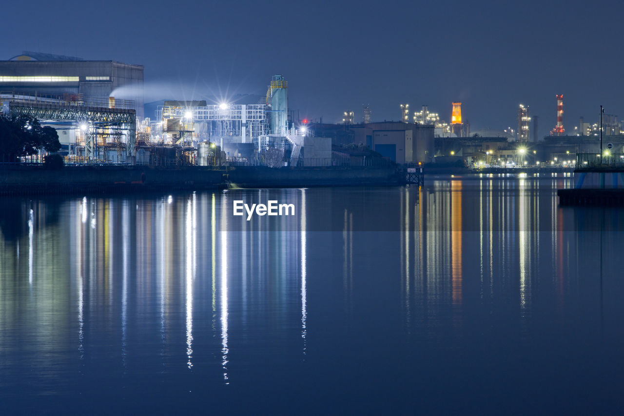 Illuminated city by sea against sky at night