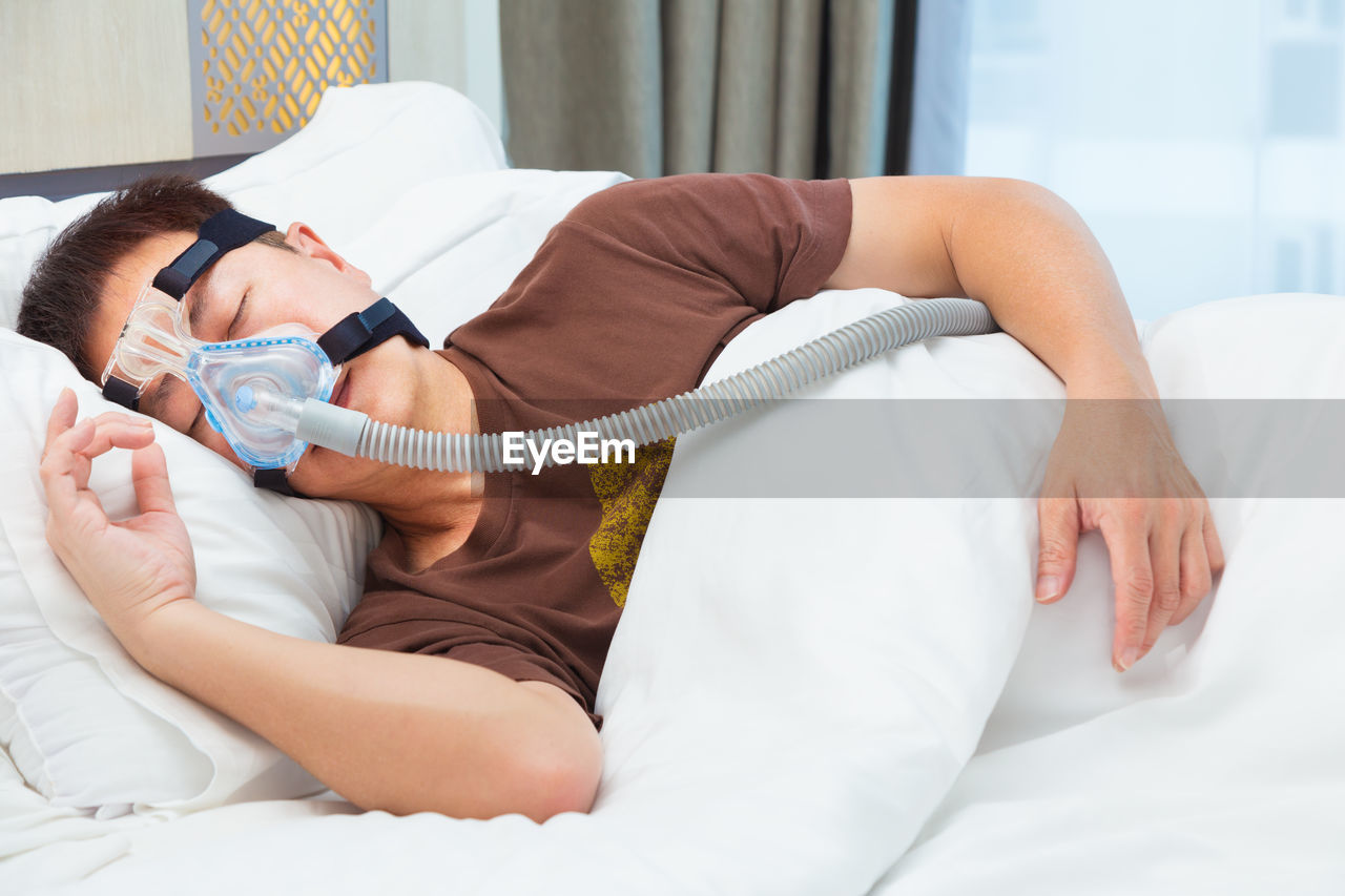 Man wearing oxygen mask while sleeping on bed at hospital