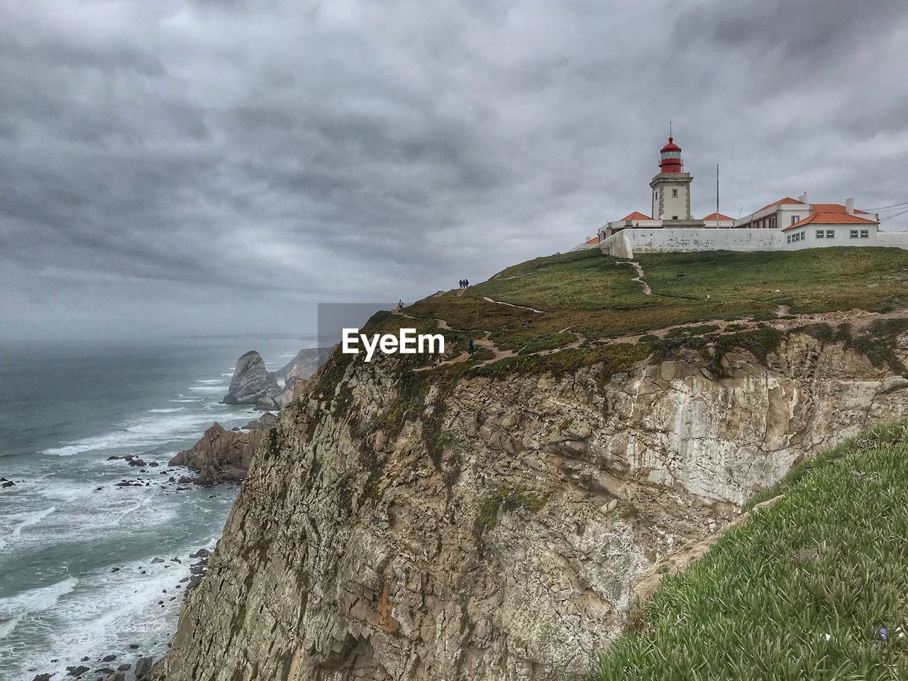 Lighthouse on mountain by sea against cloudy sky