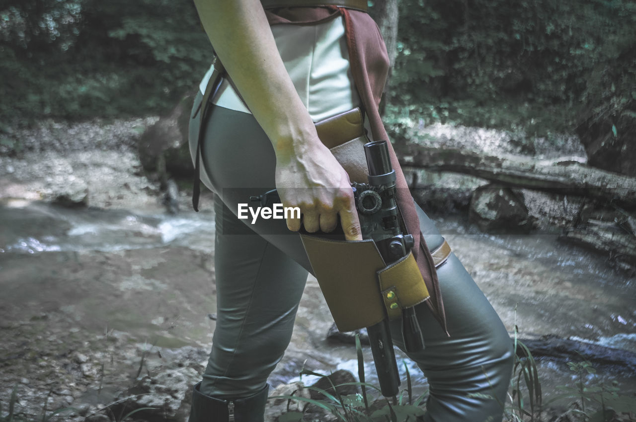 Midsection of woman with gun walking by flowing water outdoors