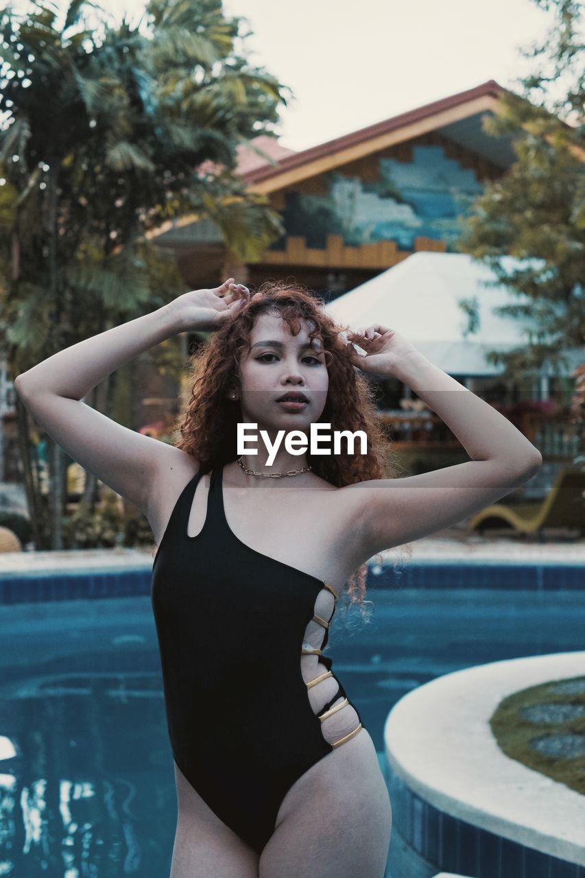 Portrait of young woman standing against swimming pool