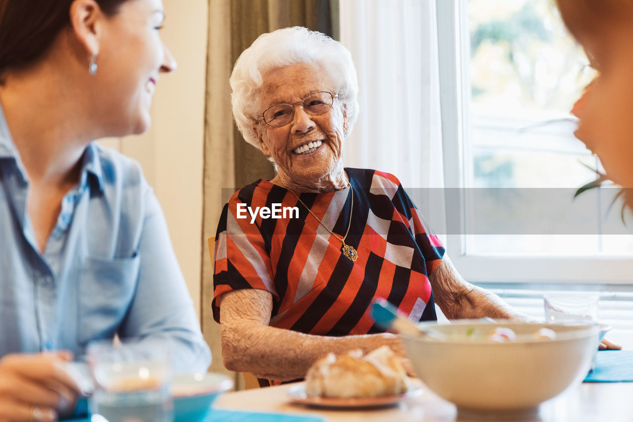 Happy senior woman talking to daughter at dining table