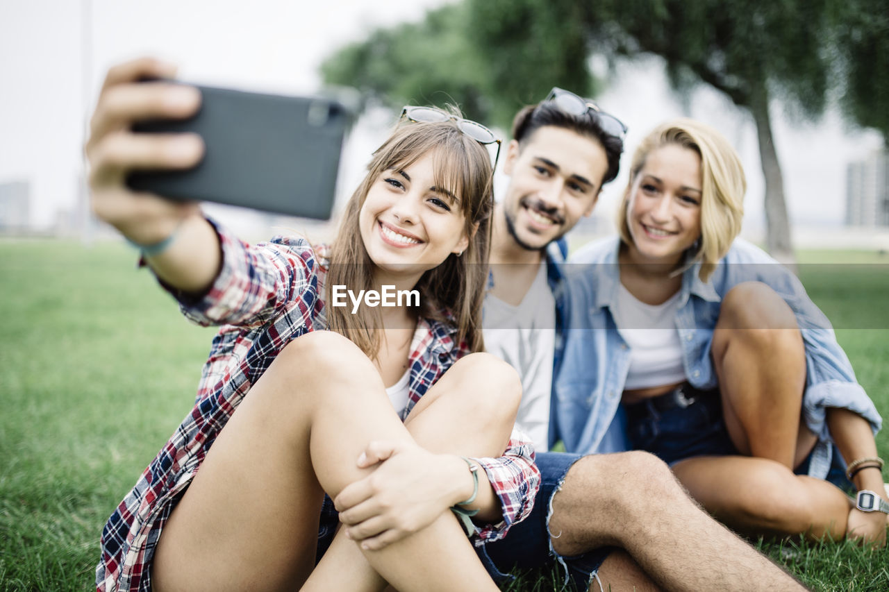 Smiling young woman with friends taking selfie on field