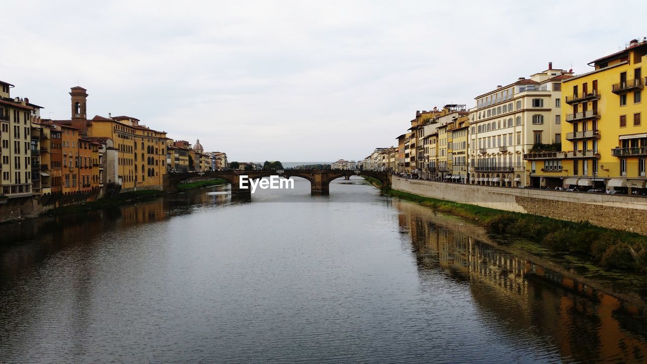 BRIDGE OVER RIVER AMIDST BUILDINGS AGAINST SKY IN CITY