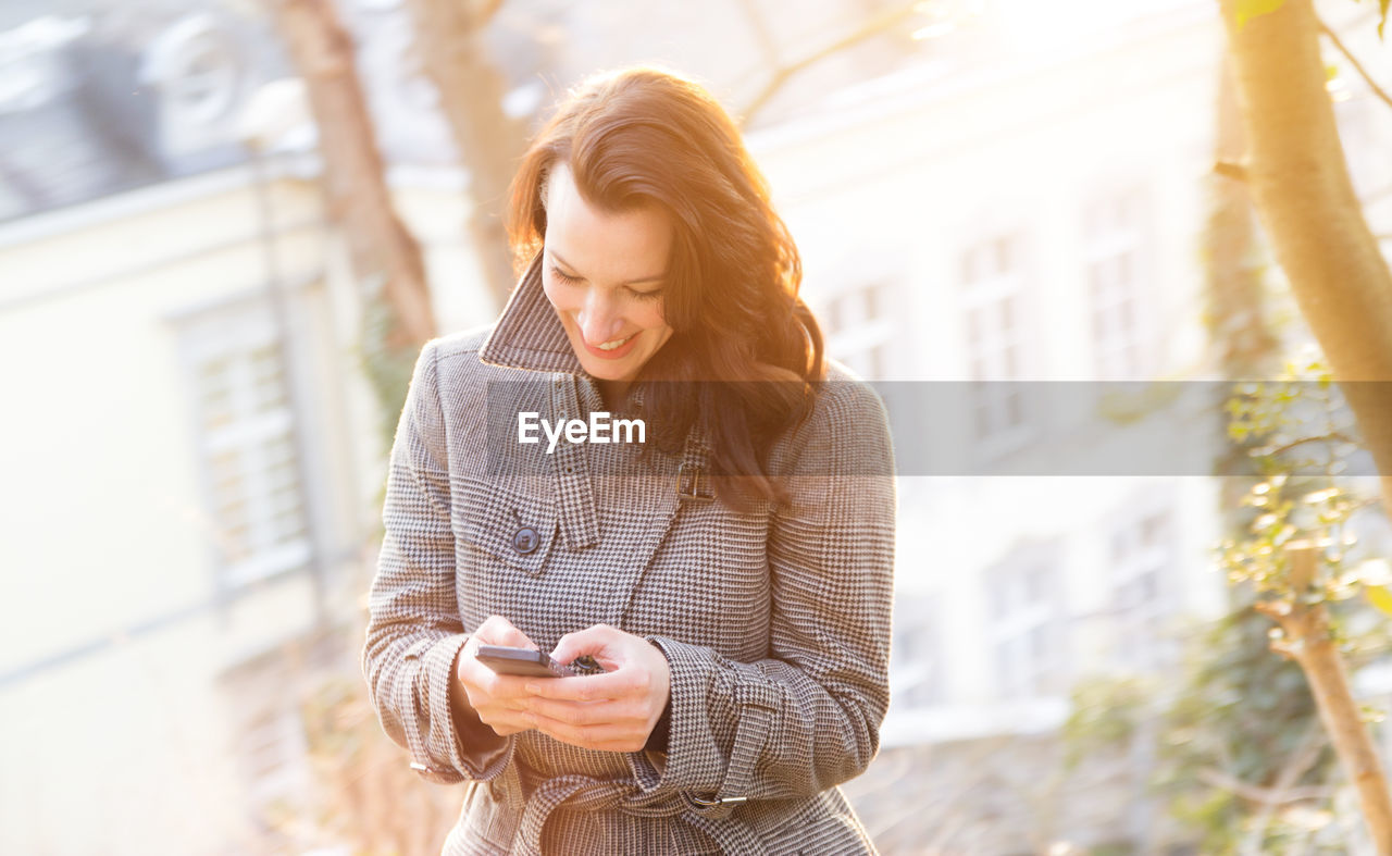 Smiling woman using phone while standing outdoors