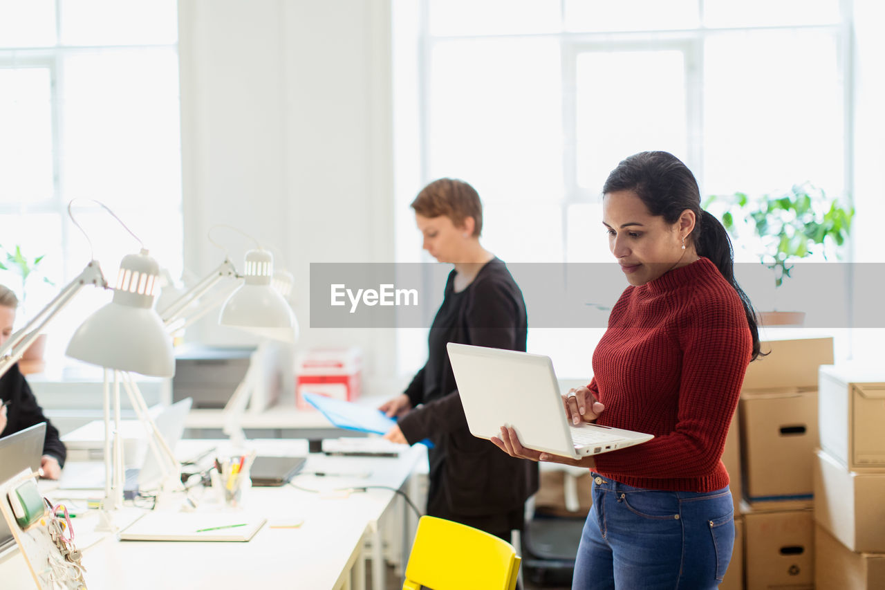 Confident businesswoman using laptop while standing at creative office