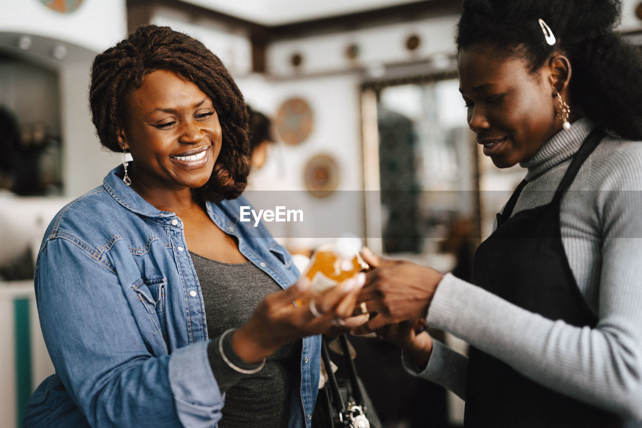 Happy female hairdresser discussing with coworker on beauty product in barber shop