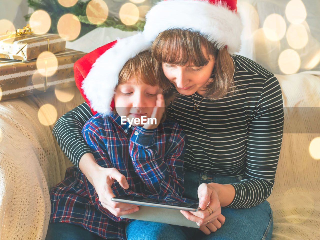 Smiling mother using digital tablet with son while sitting on sofa at home