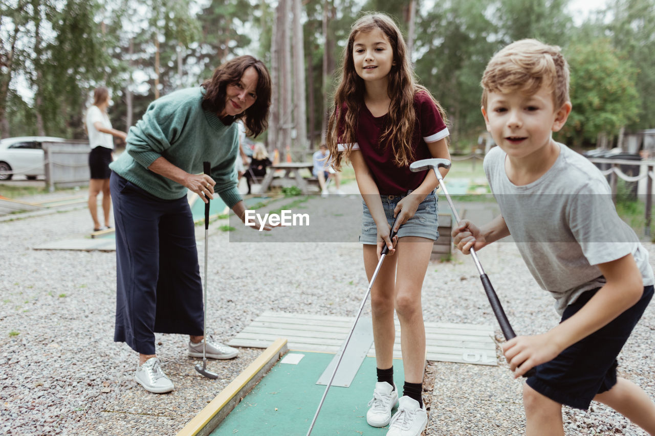 Sibling playing miniature golf with family in backyard during vacation