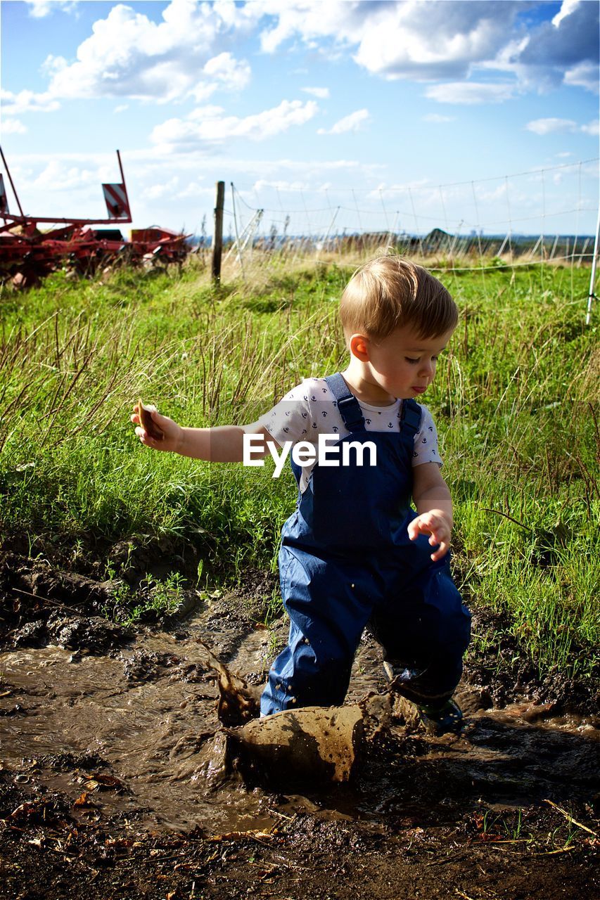 Playful boy on muddy field against sky