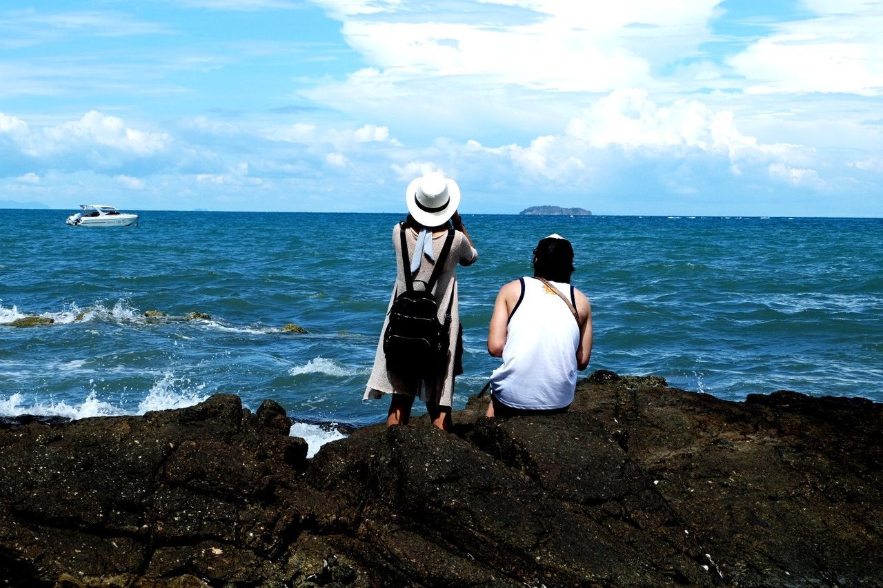 REAR VIEW OF FRIENDS STANDING ON ROCK AT BEACH