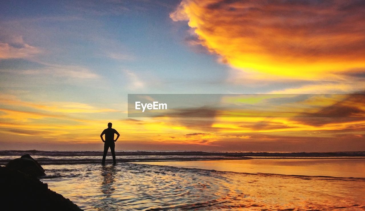 Silhouette man standing at beach against sky during sunset