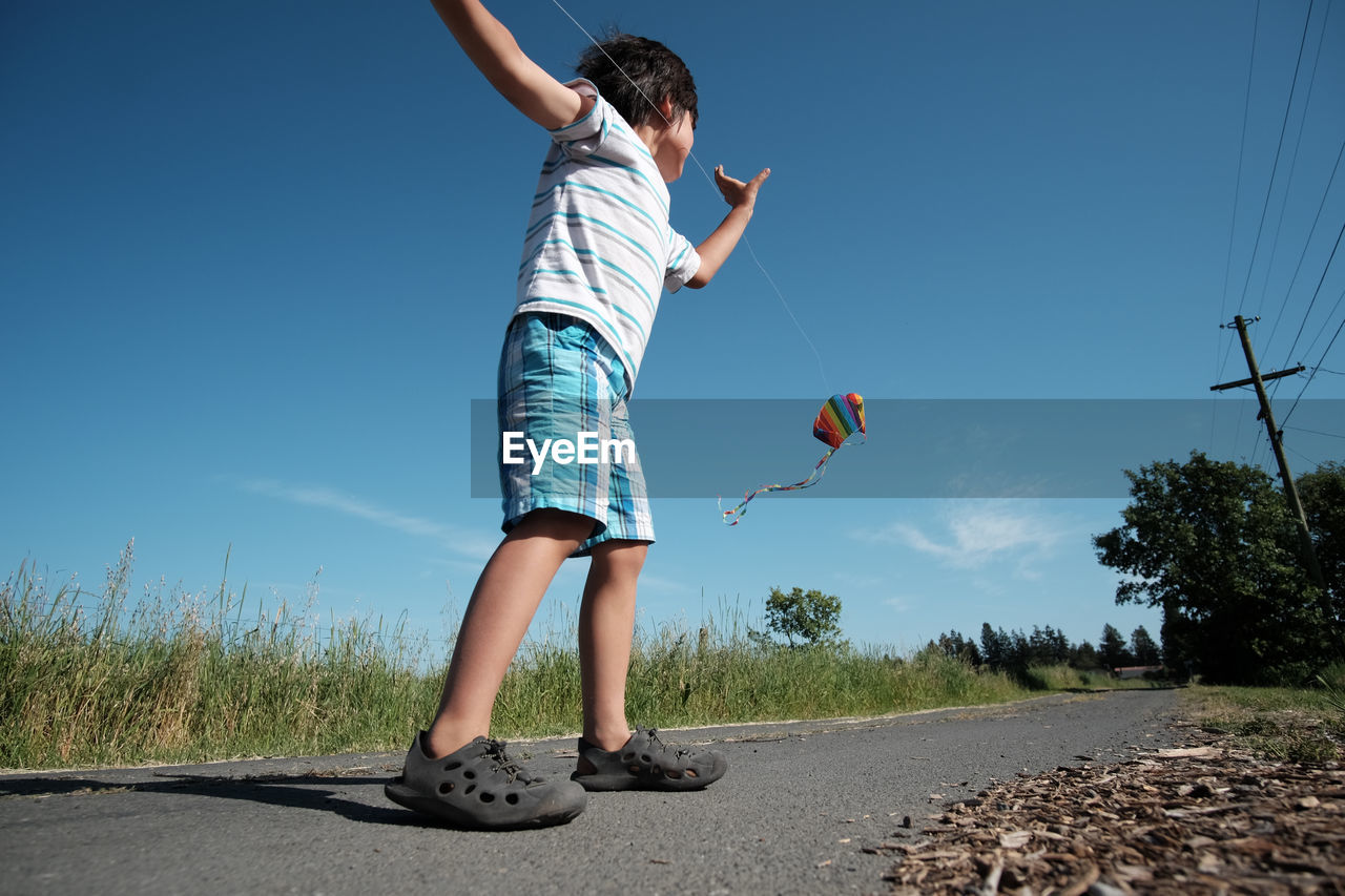 Low angle view of boy playing with kite on road against sky