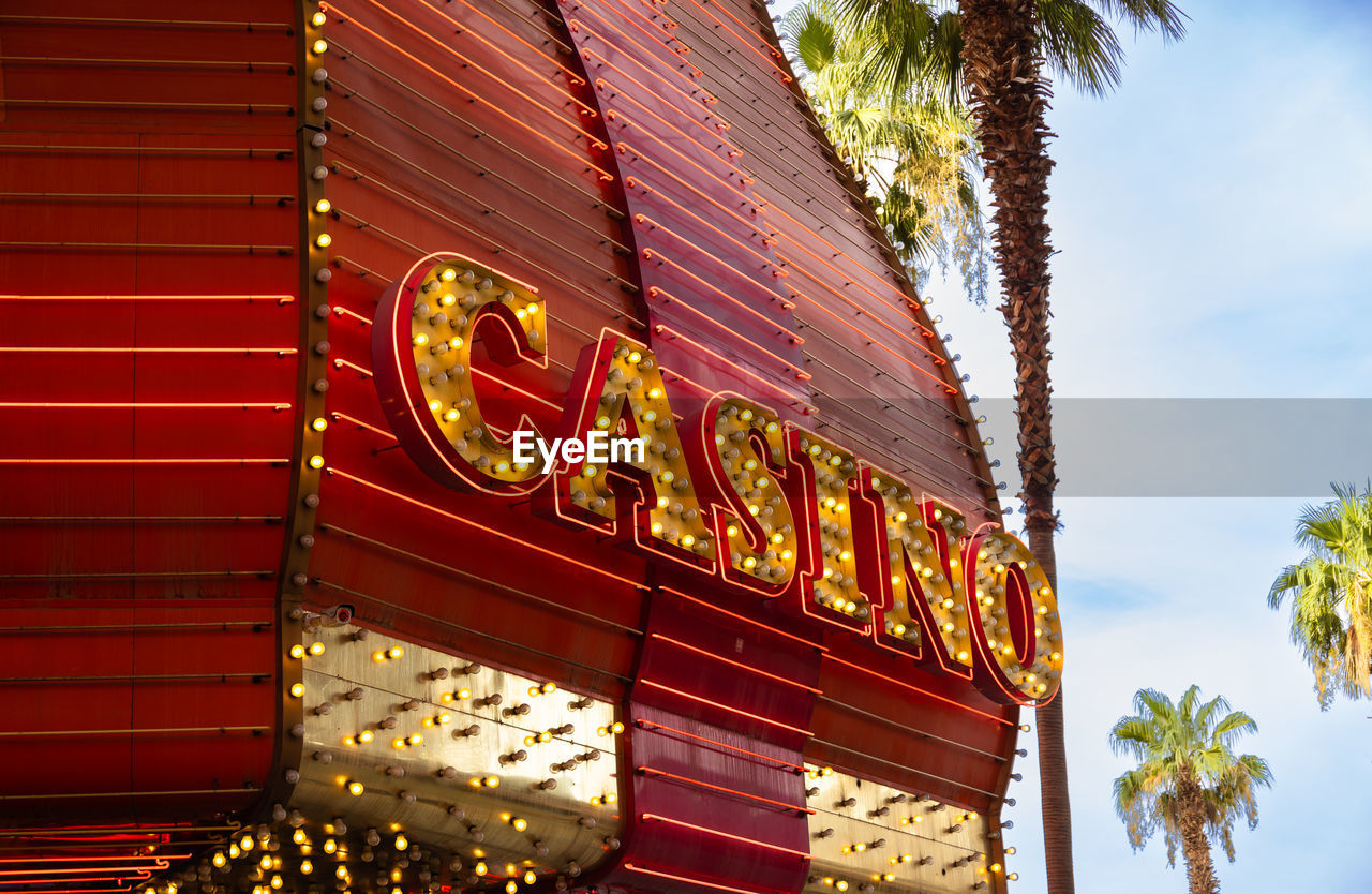 architecture, palm tree, tree, building exterior, illuminated, tropical climate, built structure, communication, text, travel destinations, nature, neon, red, no people, sign, plant, low angle view, city, sky, holiday, building, outdoors, travel, business, facade, trip, night, vacation