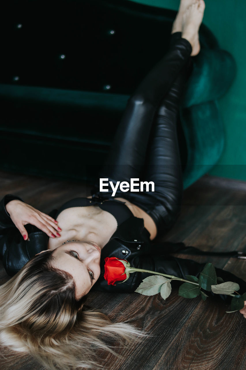 Young woman with red rose lying on floor at home