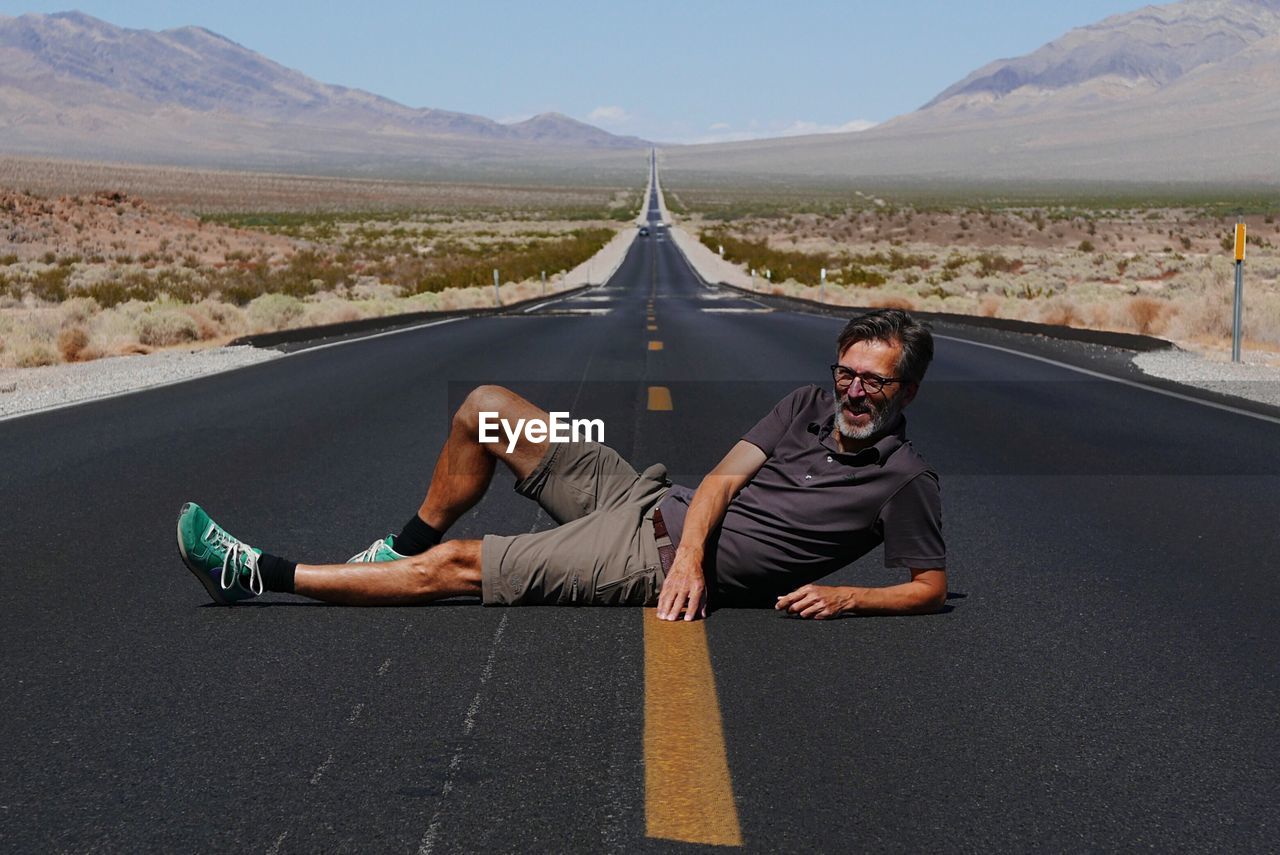 Mature man lying on road against sky