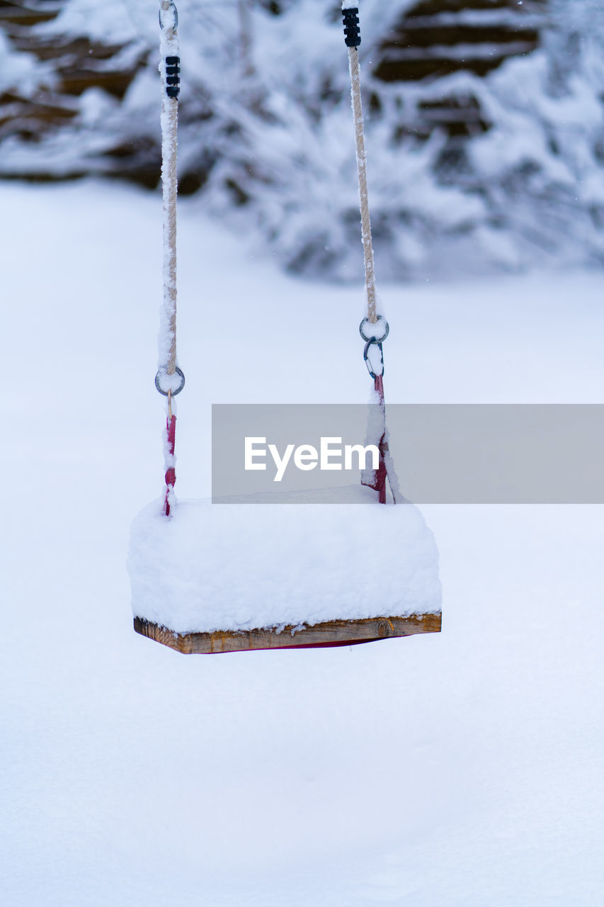 CLOSE-UP OF SNOW COVERED SWING ON FIELD