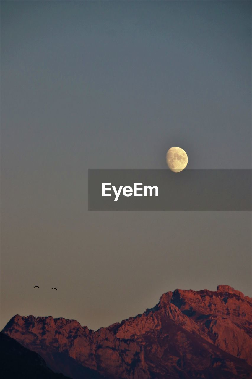 LOW ANGLE VIEW OF MOON ON MOUNTAIN AGAINST SKY