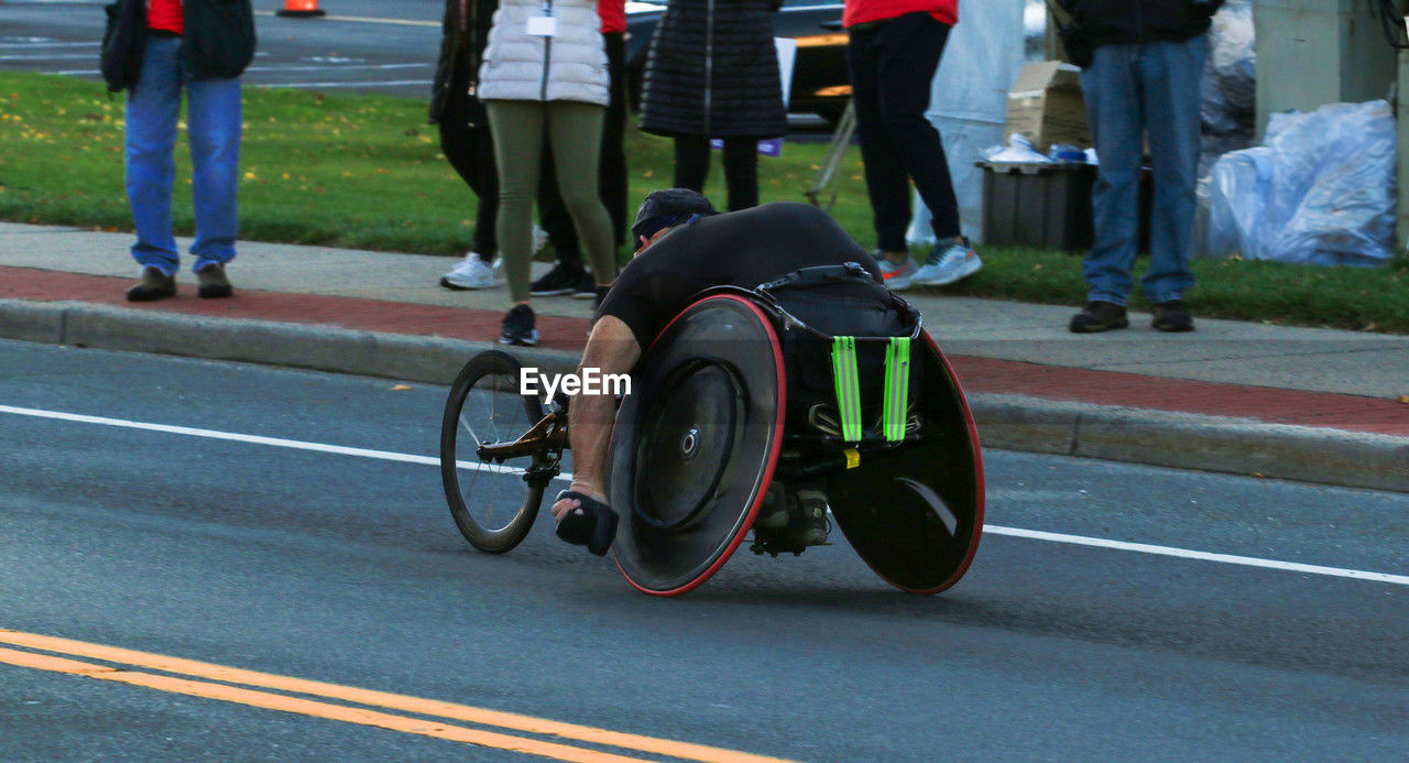 transportation, cycling, group of people, road, endurance sports, wheelchair, low section, track and field event, race, bicycle, medical equipment, road marking, vehicle, race track, city, street, wheelchair racing, differing abilities, wheel, parasports, clothing, land vehicle, day, adult, wheelchair sports, footwear, men, symbol, marking, sports, women, mode of transportation, human leg, person, outdoors, motion, bicycle racing, physical impairment