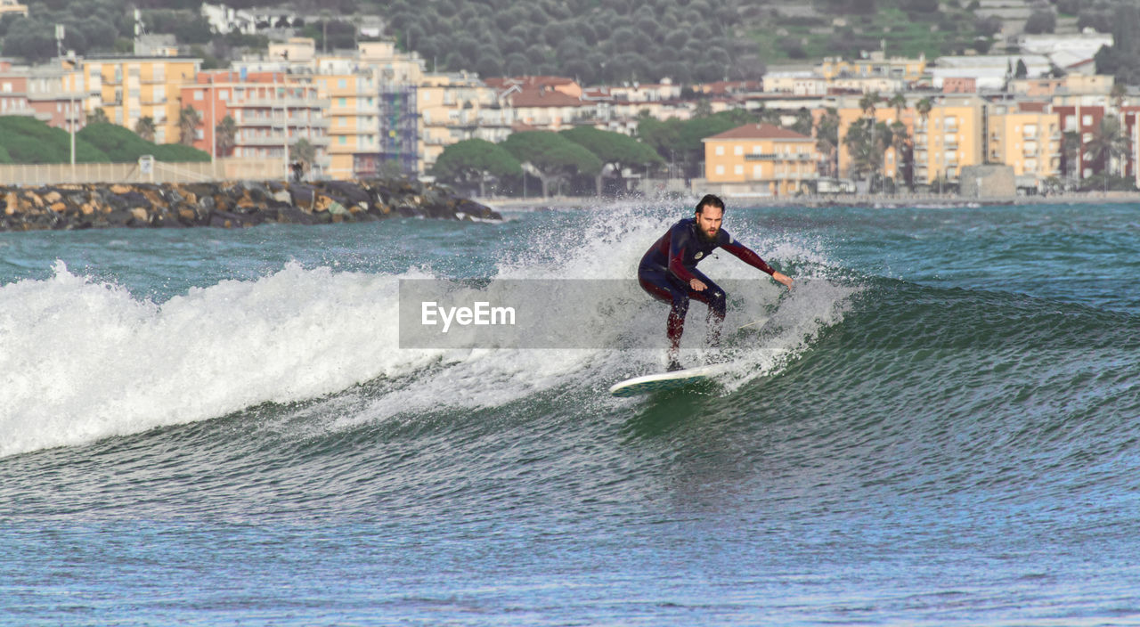 FULL LENGTH OF MAN SURFING ON CITY IN WATER