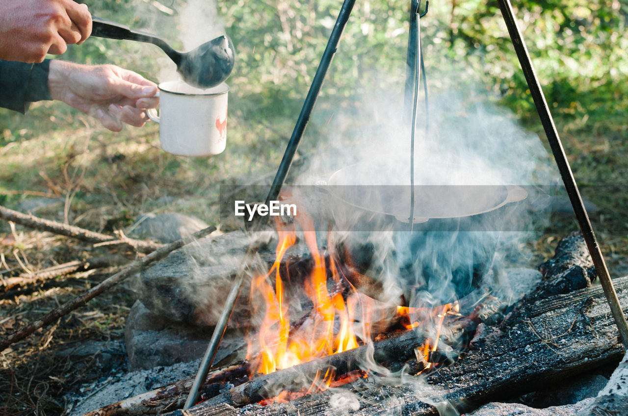 Cropped hands of person making soup on campfire in forest