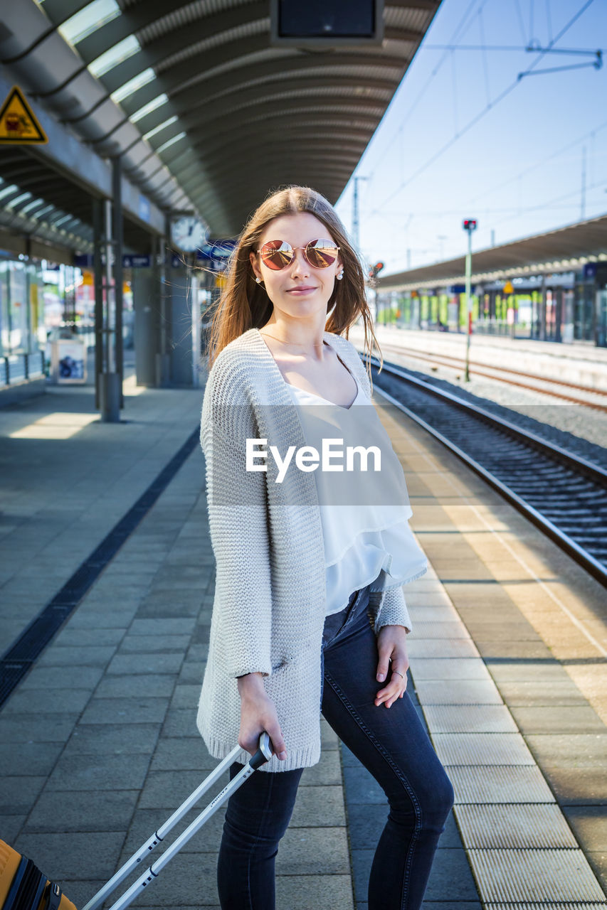 Full length of woman standing with luggage at railroad station platform