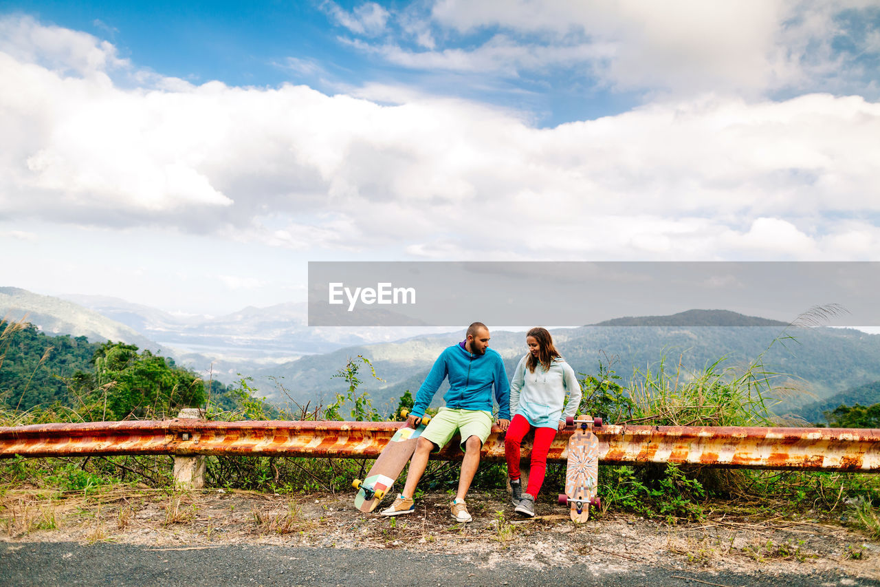 Couple sitting on railing against sky