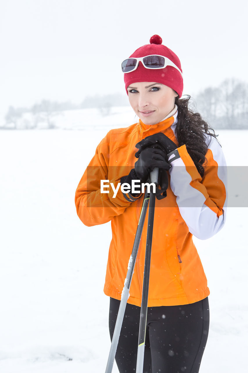 Portrait of woman holding ski poles while standing on snow covered field