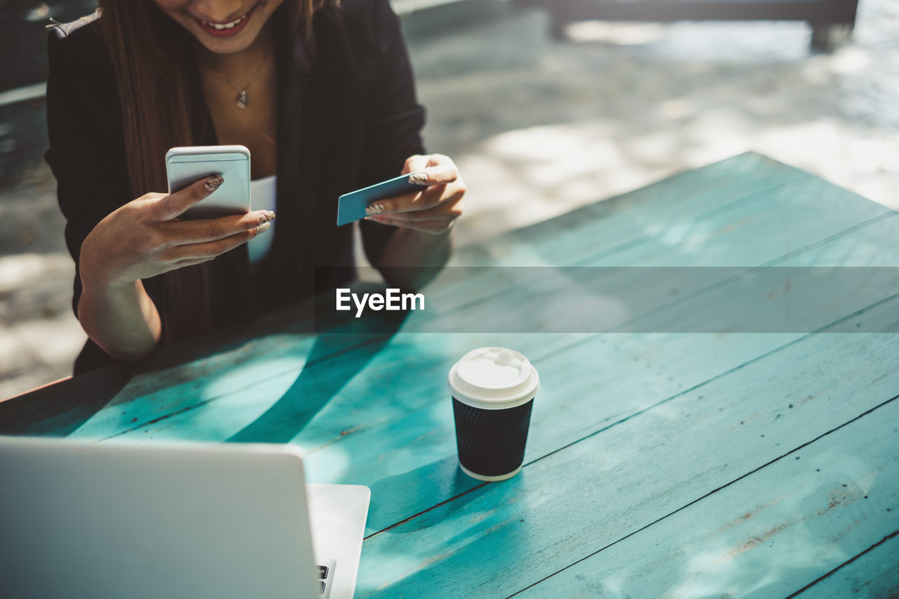 Midsection of young woman using phone while doing online shopping at table