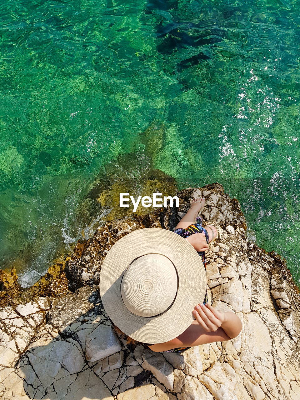 High angle view of woman on rock at beach. summer, lifestyle, sea, hat, overhead.