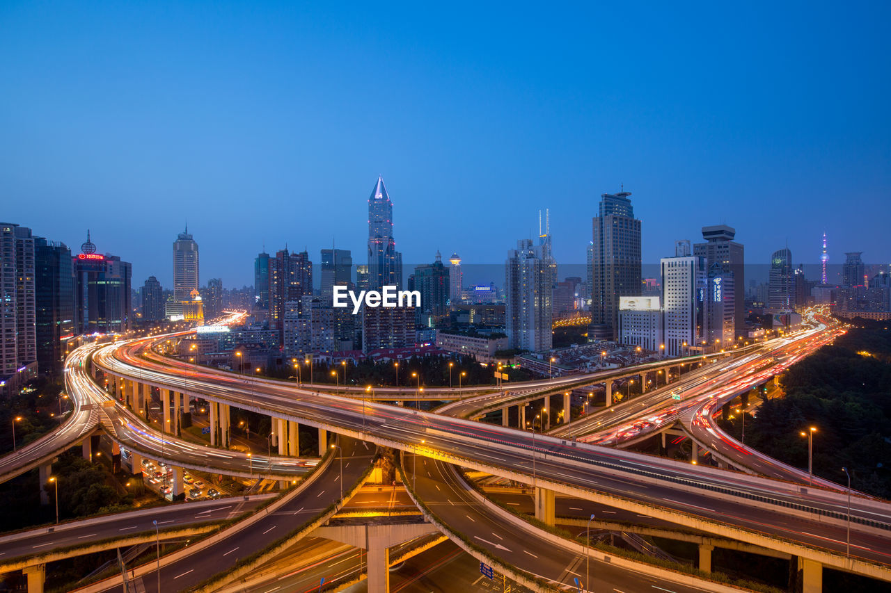 Bridges and modern buildings against clear blue sky in city at dusk