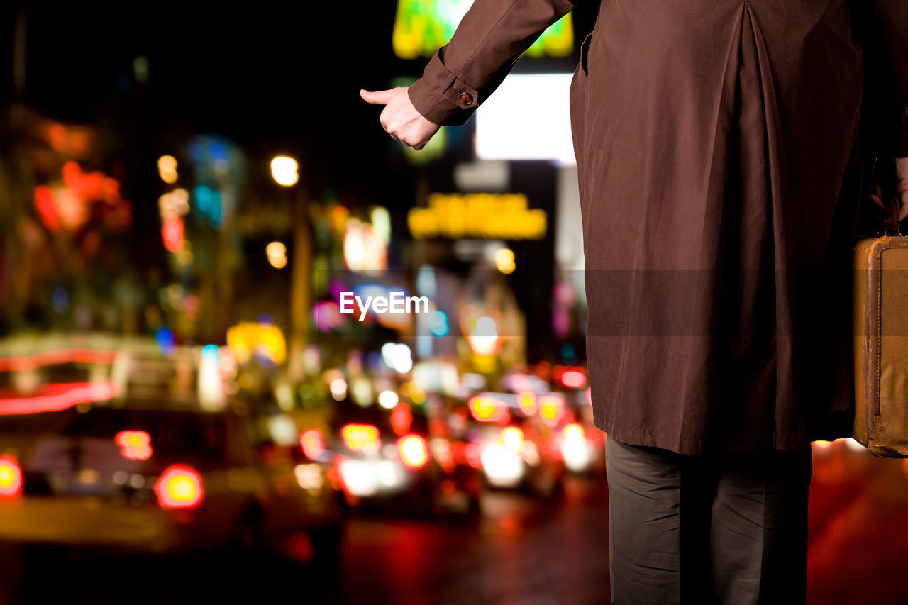 REAR VIEW OF MAN STANDING AT ILLUMINATED CITY STREET