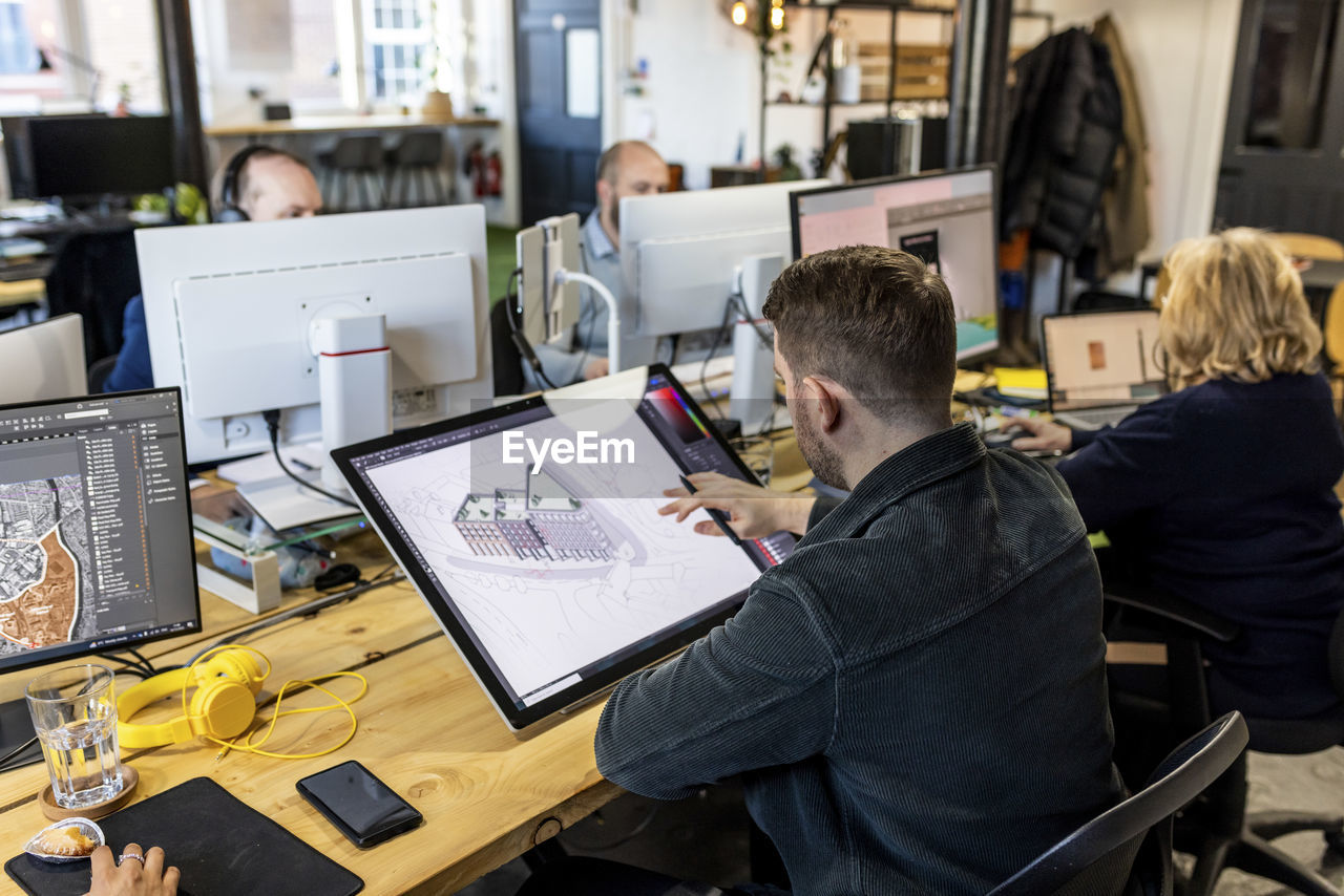 Architect working on graphics tablet with colleagues at desk in office