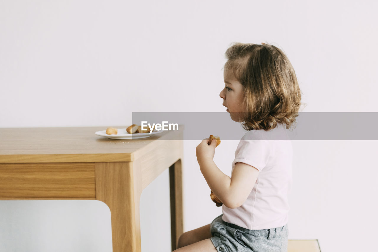A little girl sits at a table and eats cookies