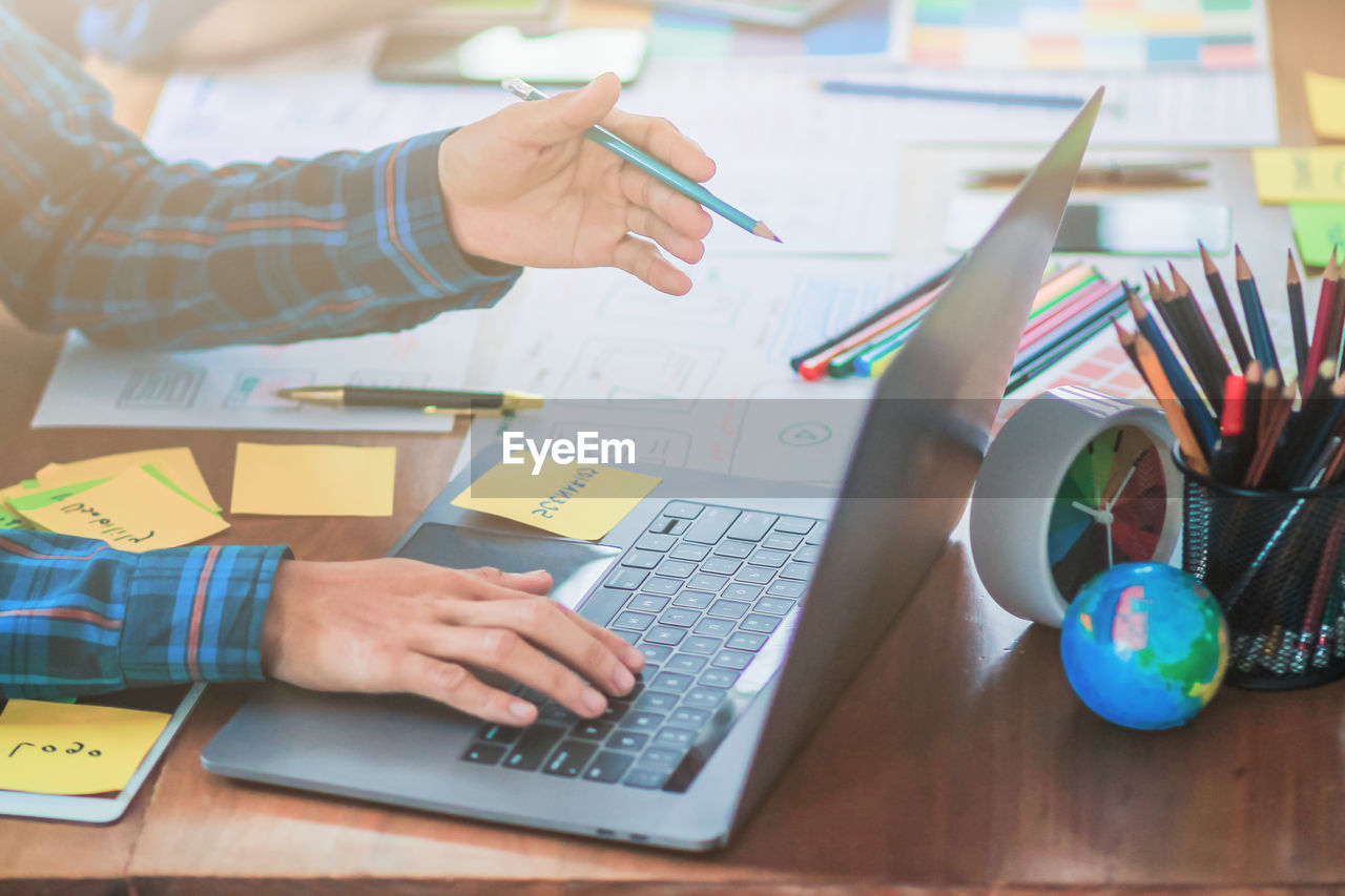 Cropped hands of businessman using laptop on desk