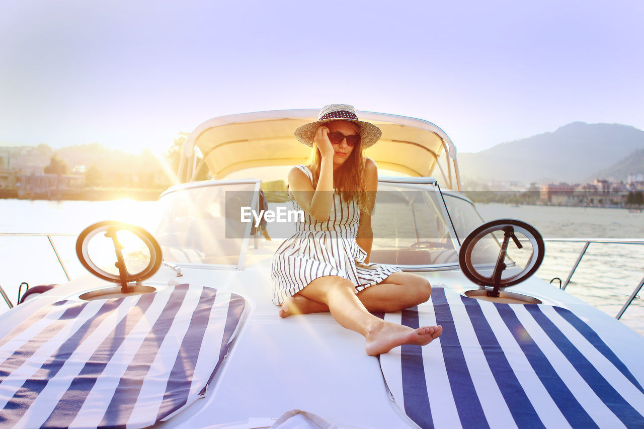 Full length of young woman sitting on boat in lake against sky