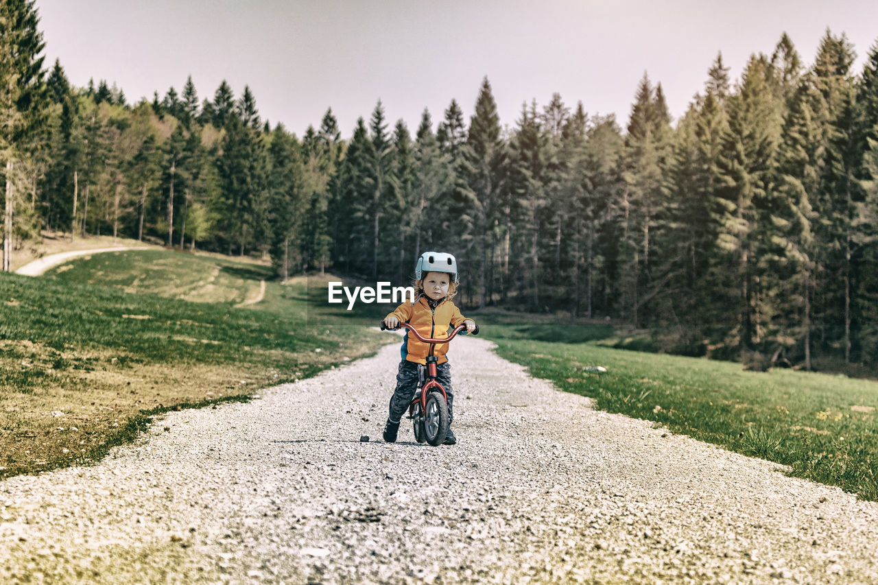 Cute girl riding bicycle on footpath against trees