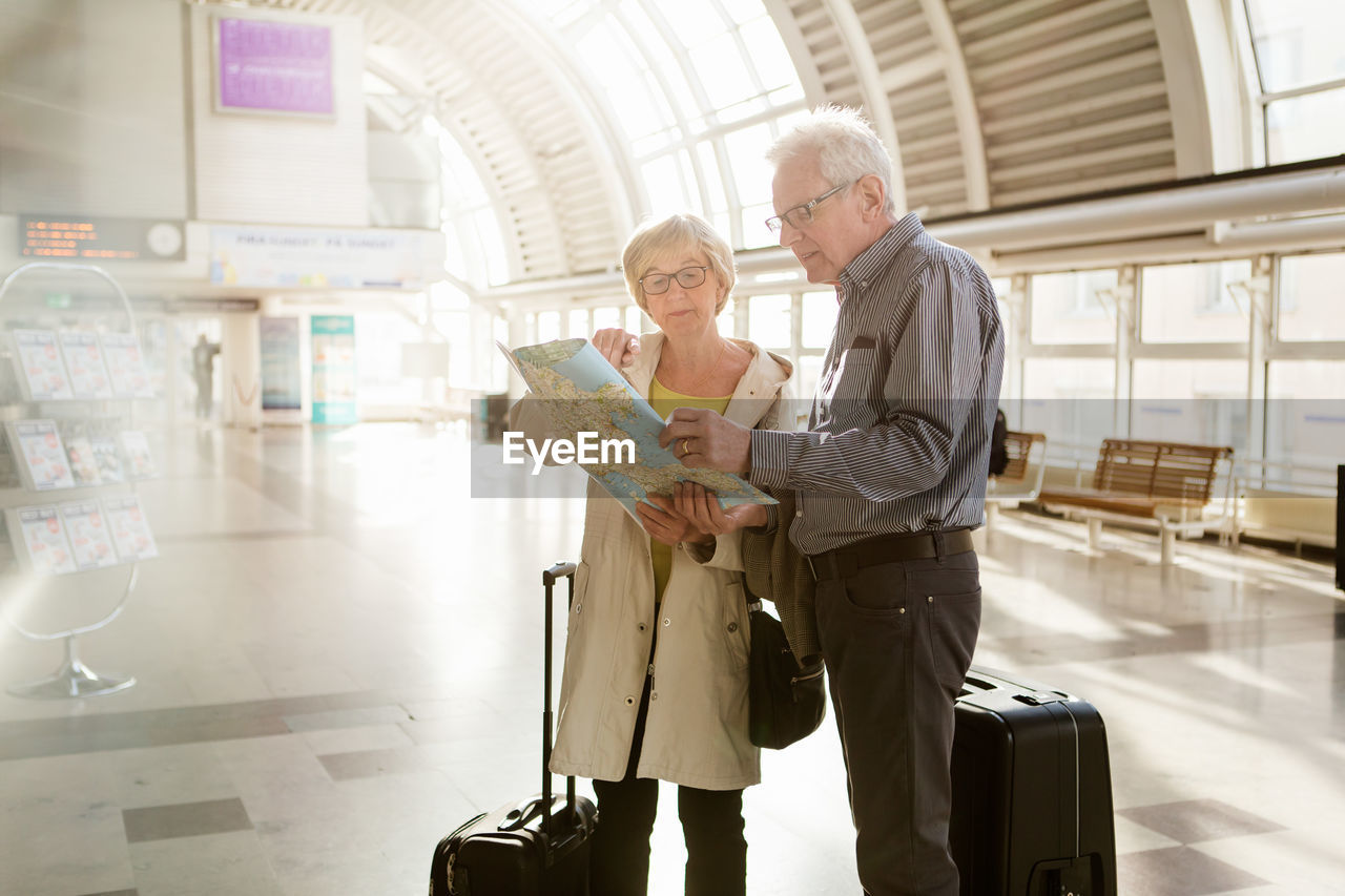 Senior woman pointing at map while standing with man on station